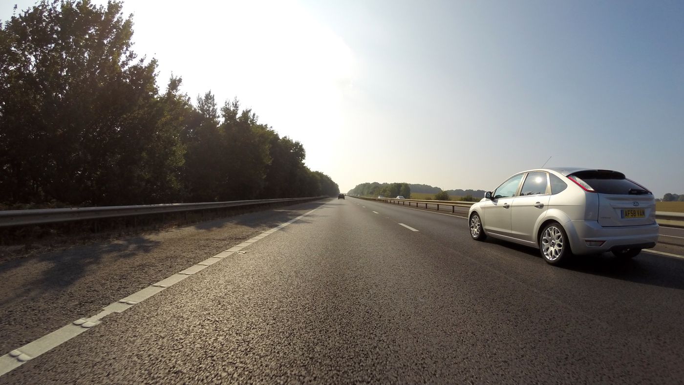 Traffic on a UK motorway in summer haze, a silver car overtaking on the right and a UK number plate in view