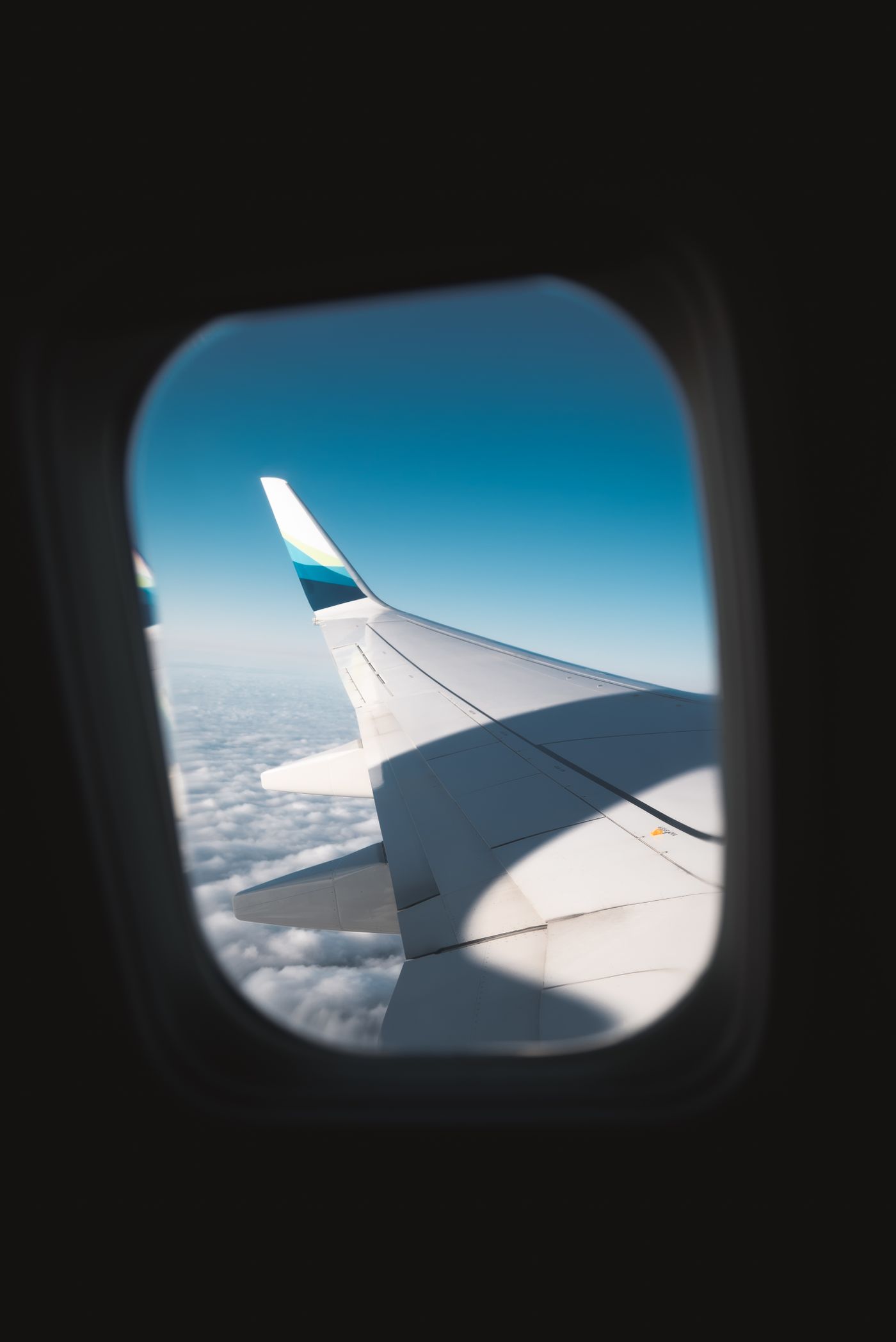 The wing and winglet of an airliner seen through a cabin window above a layer of cloud